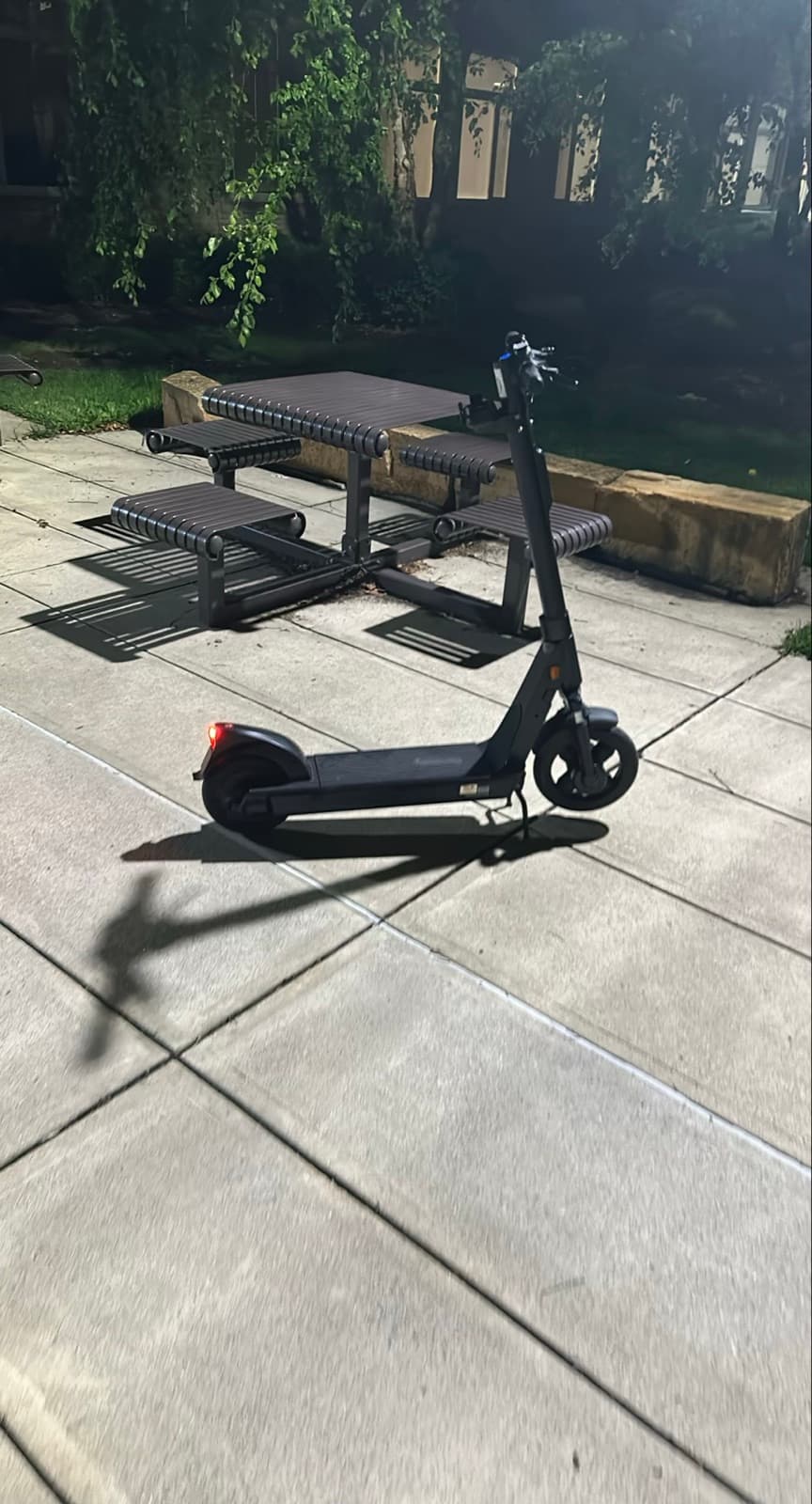 A scooter parked upright on its kickstand on open pavement, clear of walkways and entrances — an acceptable end-of-ride park